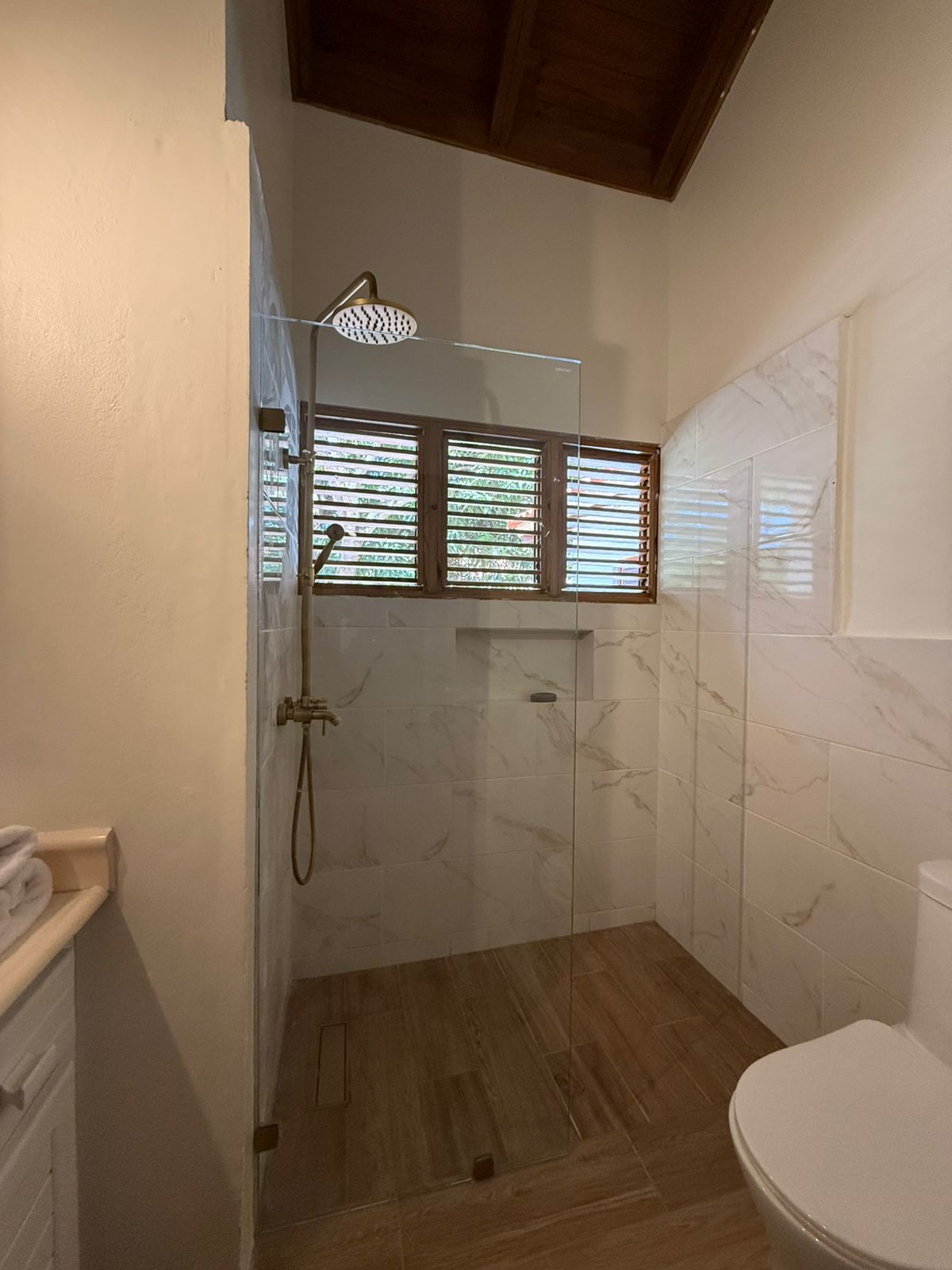 Baño de la villa con ducha de vidrio y piso con acabado de madera después de la remodelación